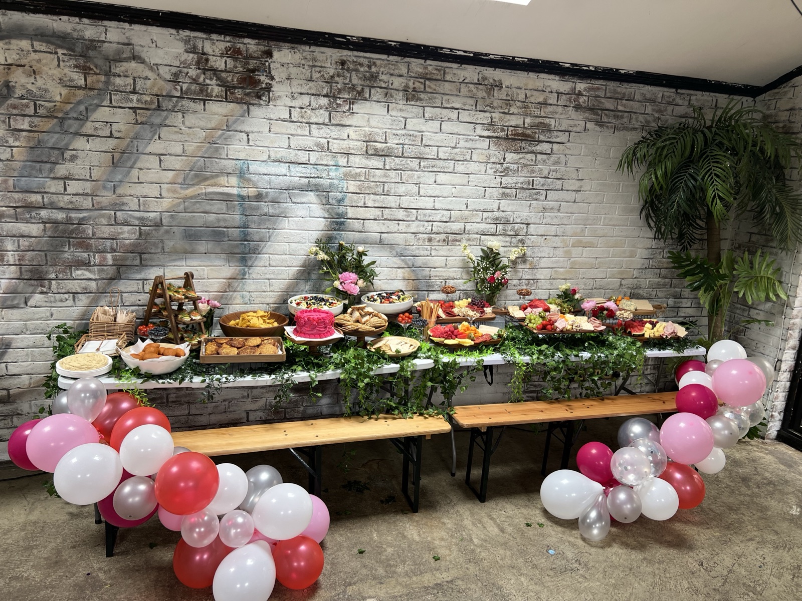Party table styled with balloons and ivy against a brick wall
